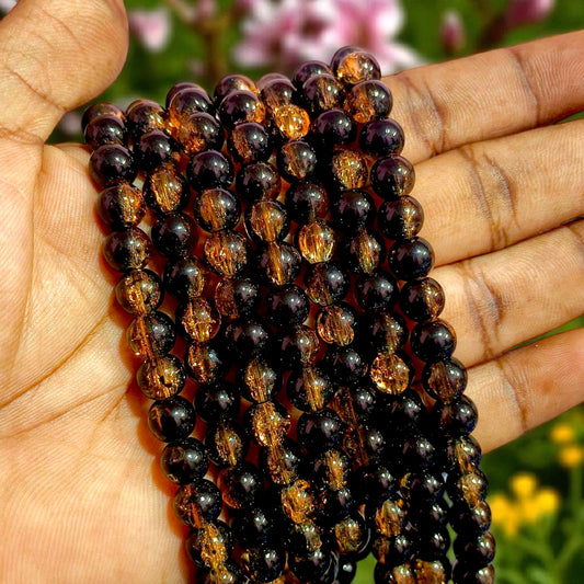 A strand of ~8 mm round crackle glass beads combining jet-black and metallic gold tones. The internal crackle fractures reflect light through translucent surfaces, creating a jewel-like, marbled shimmer