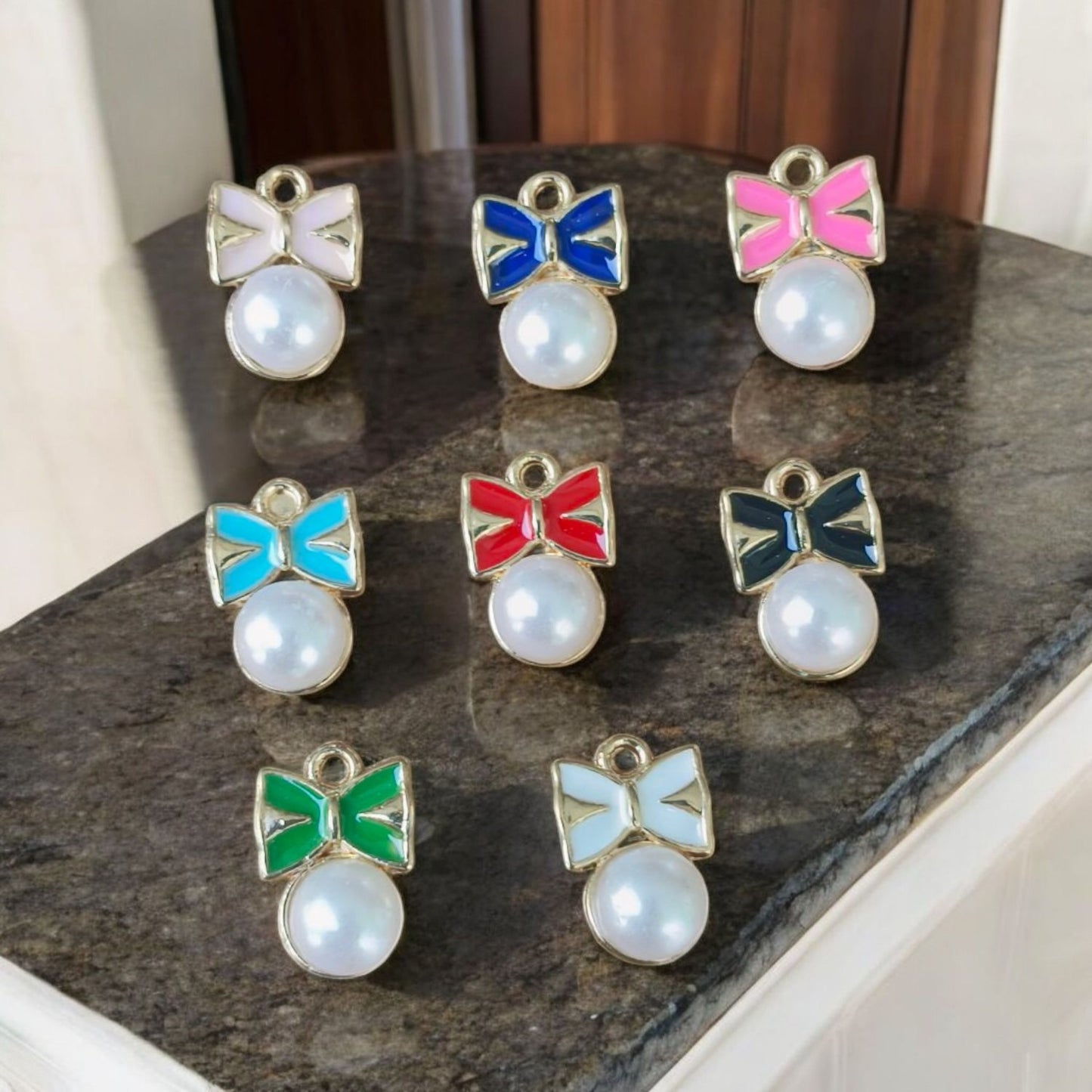 Elegant bow-shaped charms accented with dangling pearls, ideal for jewelry and craft projects.
