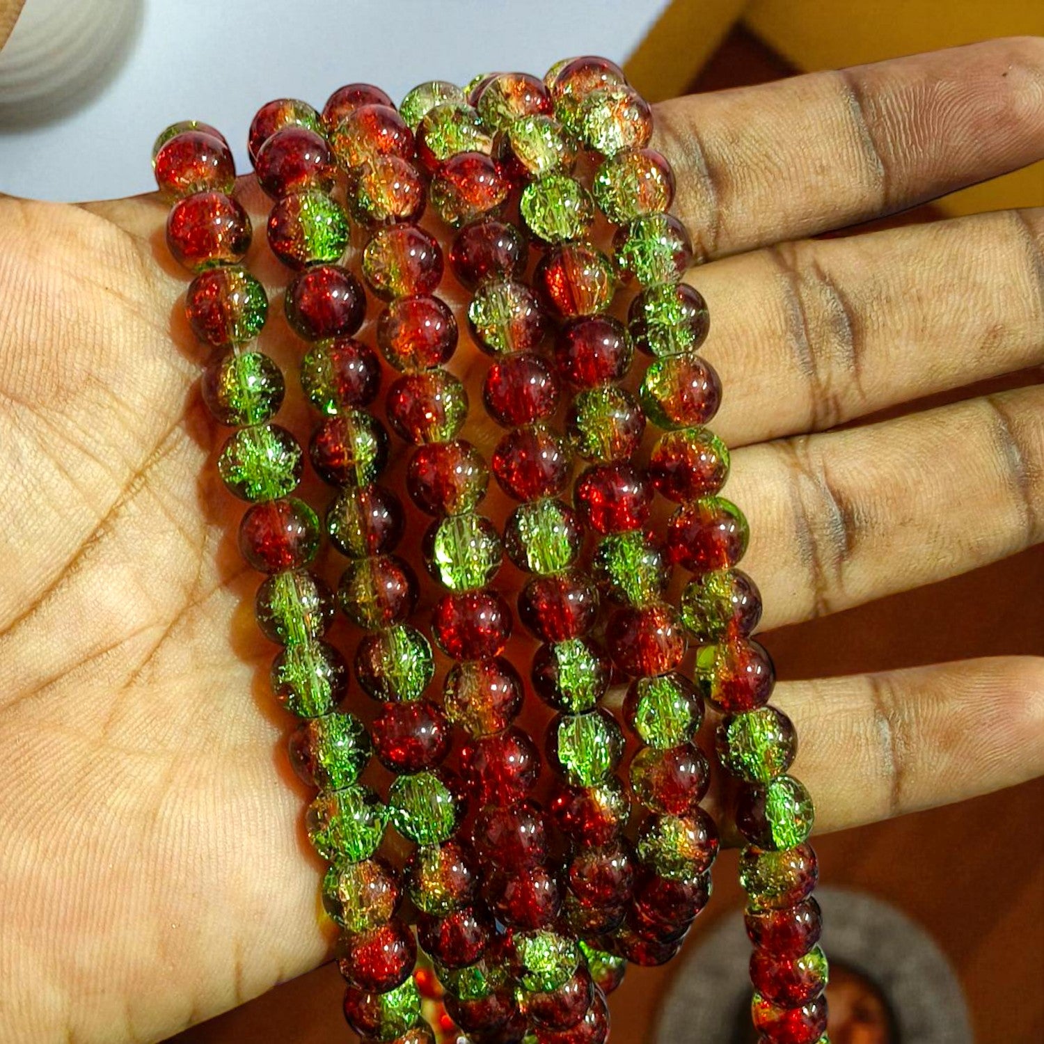 A close‑up of round glass beads in vibrant red and emerald green with a crackled interior texture that scatters light for a sparkling, mottled effect.
