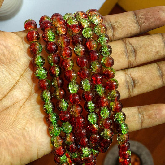 A close‑up of round glass beads in vibrant red and emerald green with a crackled interior texture that scatters light for a sparkling, mottled effect.